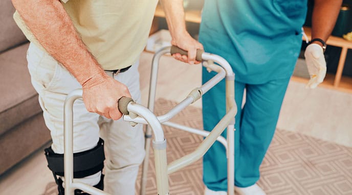 Man learning how to use a walker with help from a healthcare worker